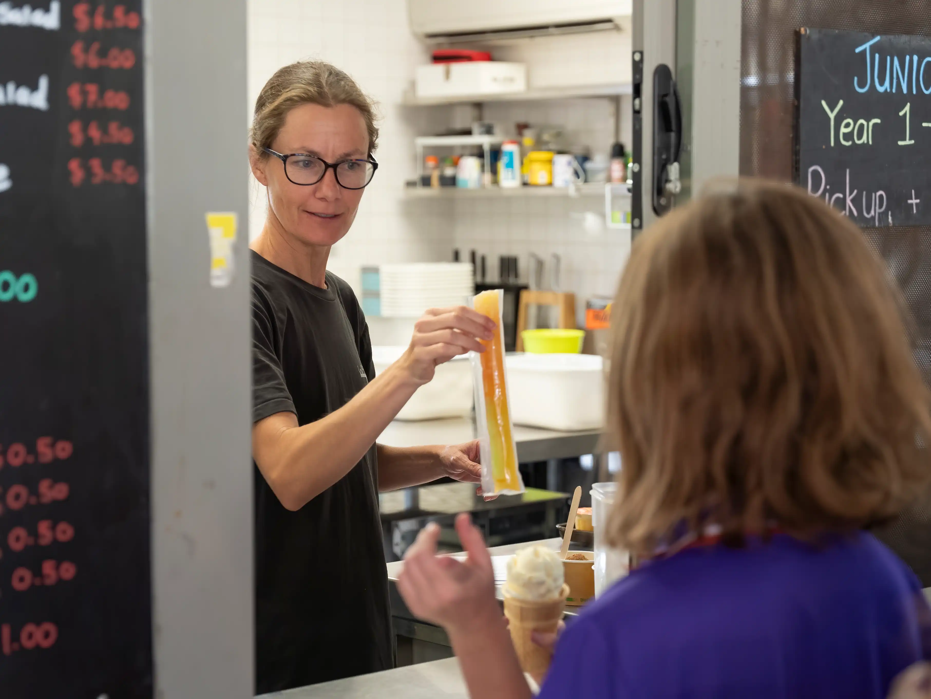 Canteen photo of a smiling woman handing a student a popsicle